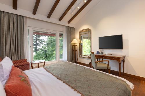 a bedroom with a bed and a desk and a television at WelcomHeritage Kasmanda Palace in Mussoorie