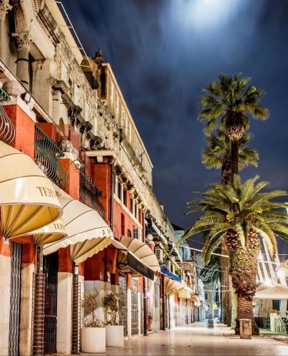a city street with two palm trees and umbrellas at Calma Luxury Rooms in Split