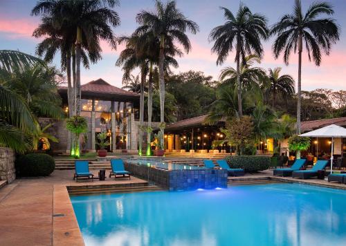 a resort pool with blue chairs and palm trees at Zimbali Lodge by Dream Resorts in Ballito