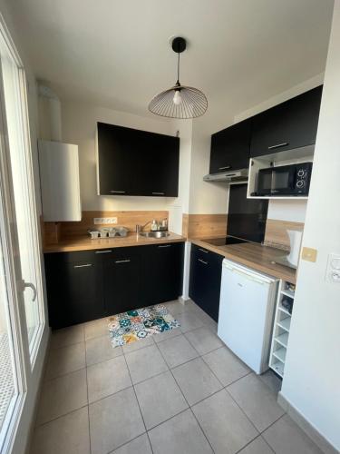 - une cuisine avec des armoires noires et un réfrigérateur blanc dans l'établissement T2 duplex au calme proche commodités, à Vaujours