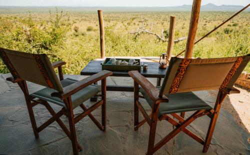 a table with two chairs and a table with a view of a field at Soroi Cheetah Tented Camp in Mwatate