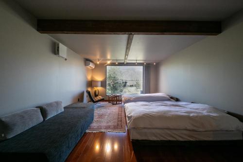 a bedroom with two beds and a couch and a window at Yufuin Kaze no Mori in Yufuin