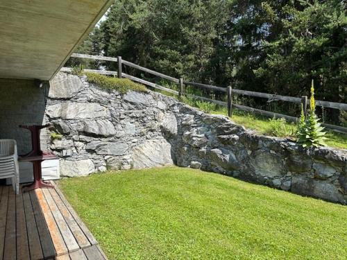 a stone wall next to a yard with a bench at Appartament ReLaax in Laax