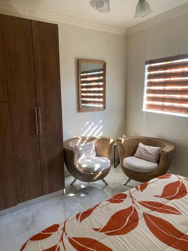 a bedroom with two chairs and a bed and a mirror at Garden Oasis Cottage in Windhoek