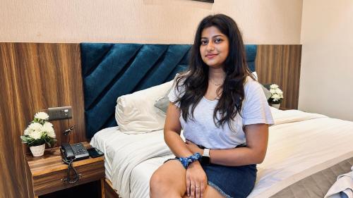 a woman sitting on a bed in a hotel room at Raksha Suites & Banquet Greater Noida in Greater Noida