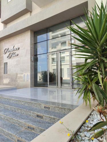 a building with glass doors and a palm tree in front at Sublime appartement le Palace Hammamet Nord Mrezga - Family only in Hammamet