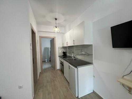 eine Küche mit weißen Schränken, einem Waschbecken und einem TV in der Unterkunft Ammos & Thalassa Apartments in Ofrynio