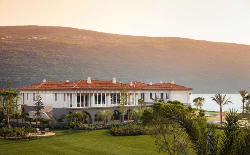 a large white house with a lawn in front of a mountain at One&Only Portonovi in Herceg-Novi