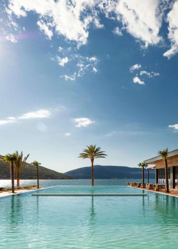 a swimming pool with palm trees and a blue sky at One&Only Portonovi in Herceg-Novi