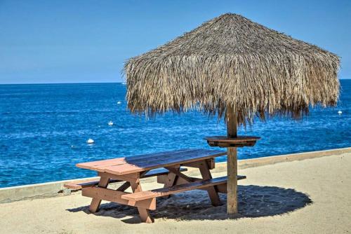 a picnic table and a straw umbrella on the beach at Oceanfront Villa With Breathtaking Views in Avalon