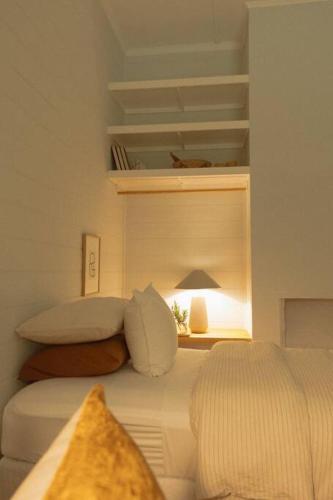 a white bedroom with a bed and a lamp at Herrings House, an iconic designer nature retreat in Willunga
