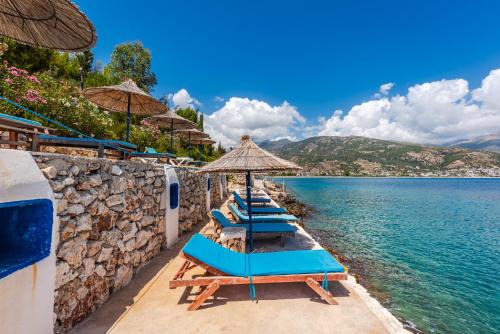 a row of beach chairs with umbrellas and the water at Stone Beach Residence - Adults Only Resort in Qeparo