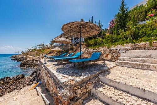 a group of chairs and an umbrella on the beach at Stone Beach Residence - Adults Only Resort in Qeparo