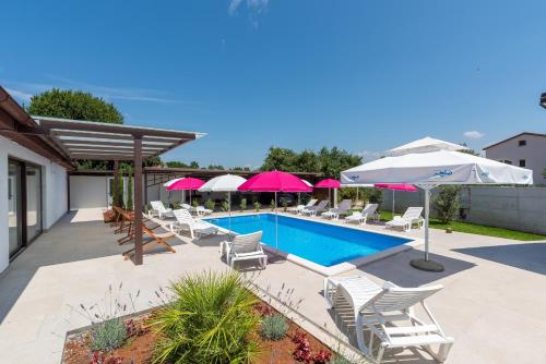 a swimming pool with white chairs and umbrellas at Nino with Shared Pool in Poreč