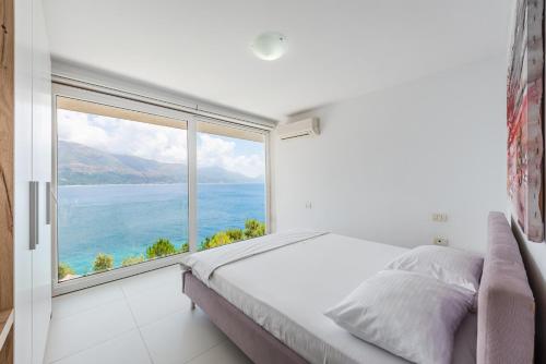 a white bedroom with a large window overlooking the water at Stone Beach Residence - Adults Only Resort in Qeparo