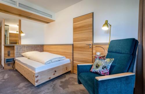a bedroom with a bed and a blue chair at Hotel FrechDachs in Bad Füssing