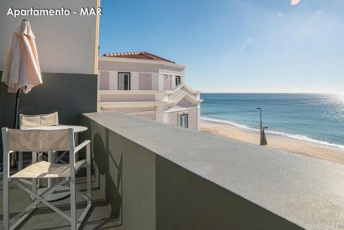 a chair and an umbrella on a balcony with the beach at Season Apartments in Sesimbra