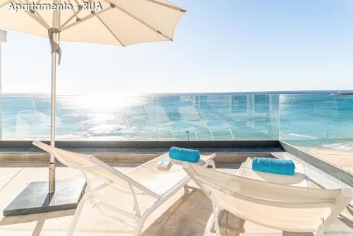 a patio with two chairs and an umbrella and the ocean at Season Apartments in Sesimbra