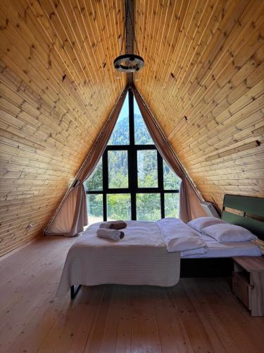 a bed in a wooden room with a large window at Borjomi Cottage Sadgeri in Sadgeri