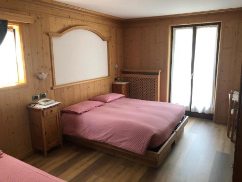 a bedroom with a bed with pink sheets and two windows at Hotel Compagnoni in Santa Caterina Valfurva