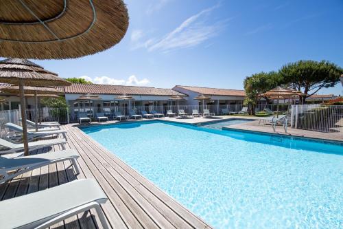 a large swimming pool with chairs and an umbrella at The Originals Boutique ,Hôtel de Ré in Sainte-Marie-de-Ré