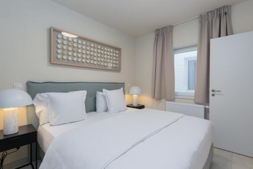 een slaapkamer met een groot wit bed en een raam bij Leader De Haan - Casselbergh Residences in De Haan