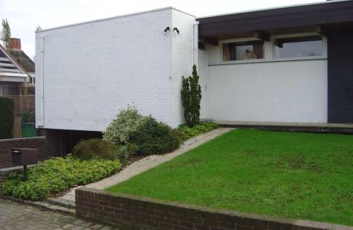 ein weißes Haus mit grünem Rasen davor in der Unterkunft Vintage Vakantiebungalow in Oostduinkerke in Koksijde