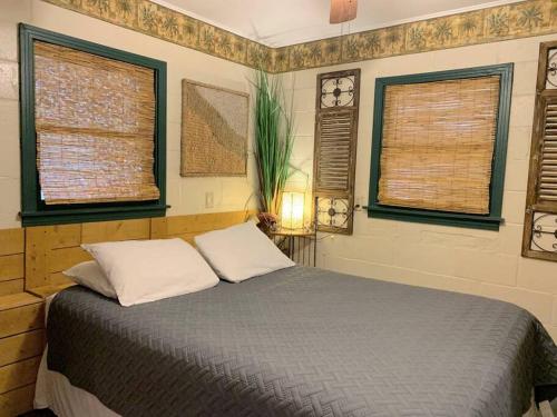 a bedroom with a bed with two pillows and two windows at The River Haven - Sleeps 32 - on Guadalupe River in Seguin