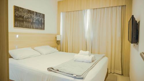 a bedroom with a bed with white sheets and a television at Beach Class Convention - Flats em Boa Viagem por Yolo in Recife