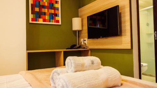 a hotel room with a bed with a television and towels at Beach Class Convention - Flats em Boa Viagem por Yolo in Recife