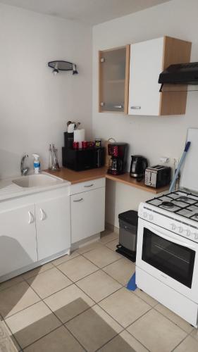 une cuisine avec des armoires blanches et un four à plaques de cuisson dans l'établissement Appartement 4 couchages - Centre ville St Donat sur l'Herbasse, à Saint-Donat-sur-lʼHerbasse