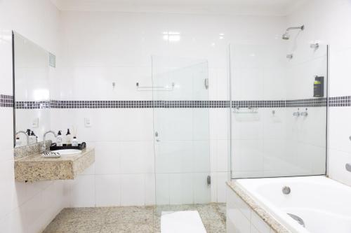 a white bathroom with a tub and a sink at BOMBONATO HOTEL - Fácil Acesso ao Aeroporto e parque de Exposições ABCZ in Uberaba