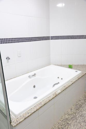 a white bathroom with a large tub in it at BOMBONATO HOTEL - Fácil Acesso ao Aeroporto e parque de Exposições ABCZ in Uberaba
