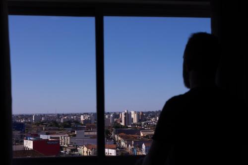 a person looking out a window at a city at BOMBONATO HOTEL - Fácil Acesso ao Aeroporto e parque de Exposições ABCZ in Uberaba