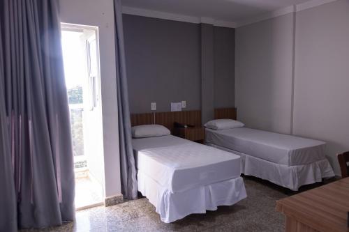 two beds in a room with a window at BOMBONATO HOTEL - Fácil Acesso ao Aeroporto e parque de Exposições ABCZ in Uberaba