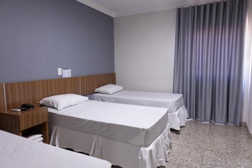 a room with three beds with white sheets at BOMBONATO HOTEL - Fácil Acesso ao Aeroporto e parque de Exposições ABCZ in Uberaba