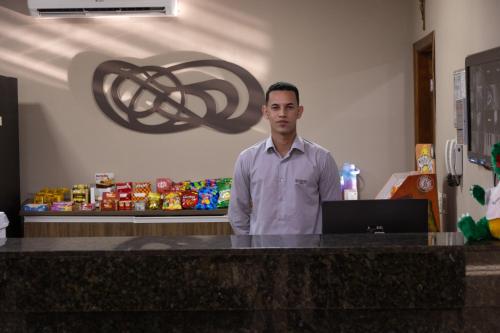 a man standing in front of a counter with a laptop at BOMBONATO HOTEL - Fácil Acesso ao Aeroporto e parque de Exposições ABCZ in Uberaba