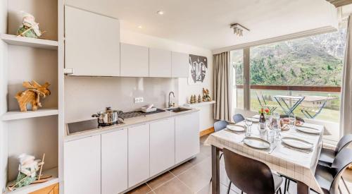 une cuisine avec des armoires blanches et une table avec des chaises dans l'établissement Résidence Combe Folle - 2 Pièces pour 6 Personnes MAE-6854, à Tignes