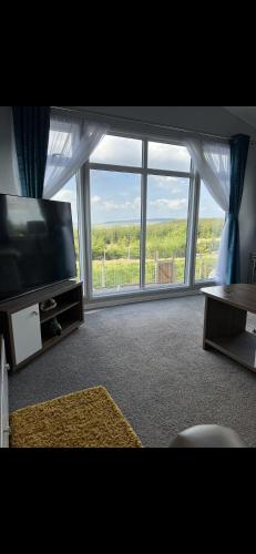 a living room with a tv and a large window at Maneight Retreat in New Cumnock