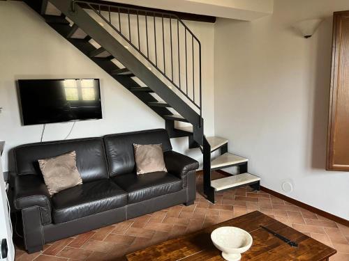 un soggiorno con divano in pelle nera e scala di House in Tuscany - Casa La Scala a Gaiole in Chianti
