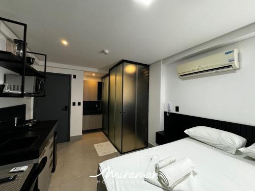 a bedroom with a white bed and a kitchen at Get By Side - Jardim Oceania in Tambaú