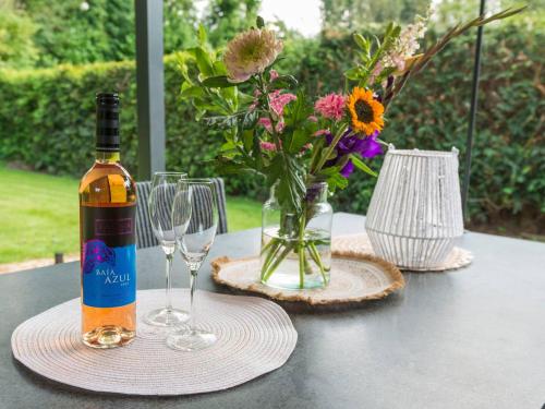 a bottle of wine and glasses on a table with flowers at Goldenescape 6P Vip huis met Royale tuin en hottub 110 in Ewijk