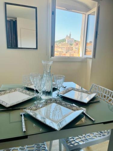 une table avec des verres, des assiettes et une fenêtre dans l'établissement T2 au pied du Vieux port et vue Notre Dame, à Marseille