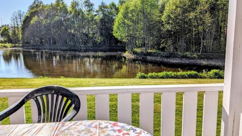 a table and chair on a porch with a view of a river at Rolig häst, Kaneeling Stugby AB in Dalskog