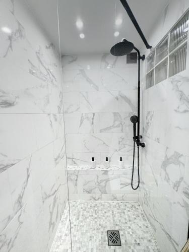 La salle de bains est pourvue d'une douche et de murs en marbre blanc. dans l'établissement Luxe Évasion avec vue incroyable, parking gratuit, à Maisons-Alfort