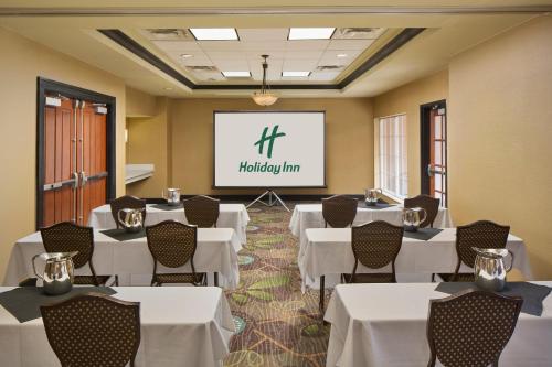 a conference room with white tables and chairs and a screen at Holiday Inn Grand Rapids-Airport by IHG in Grand Rapids