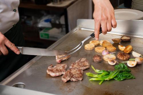 a person is cooking meat and vegetables on a grill at Hotel Continental Fuchu in Fuchu