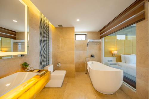 a bathroom with a large white tub and a bedroom at Mandila Beach Hotel Danang in Da Nang