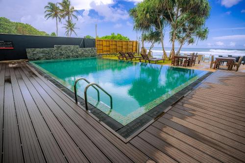 a swimming pool with a wooden deck and the ocean at Beach & Bliss Mirissa in Mirissa