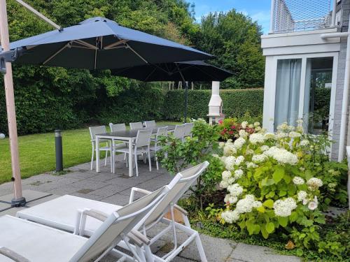 a patio with white chairs and an umbrella and flowers at Ferienparadies Seeluft in Kamperland